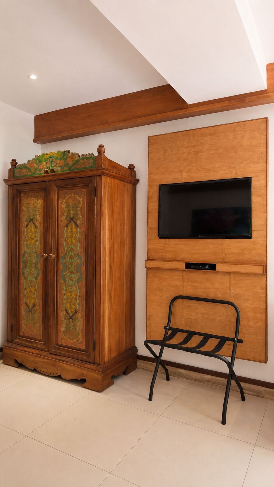 Une pièce comprenant un meuble en bois, un téléviseur fixé au mur et une chaise pliante en métal.