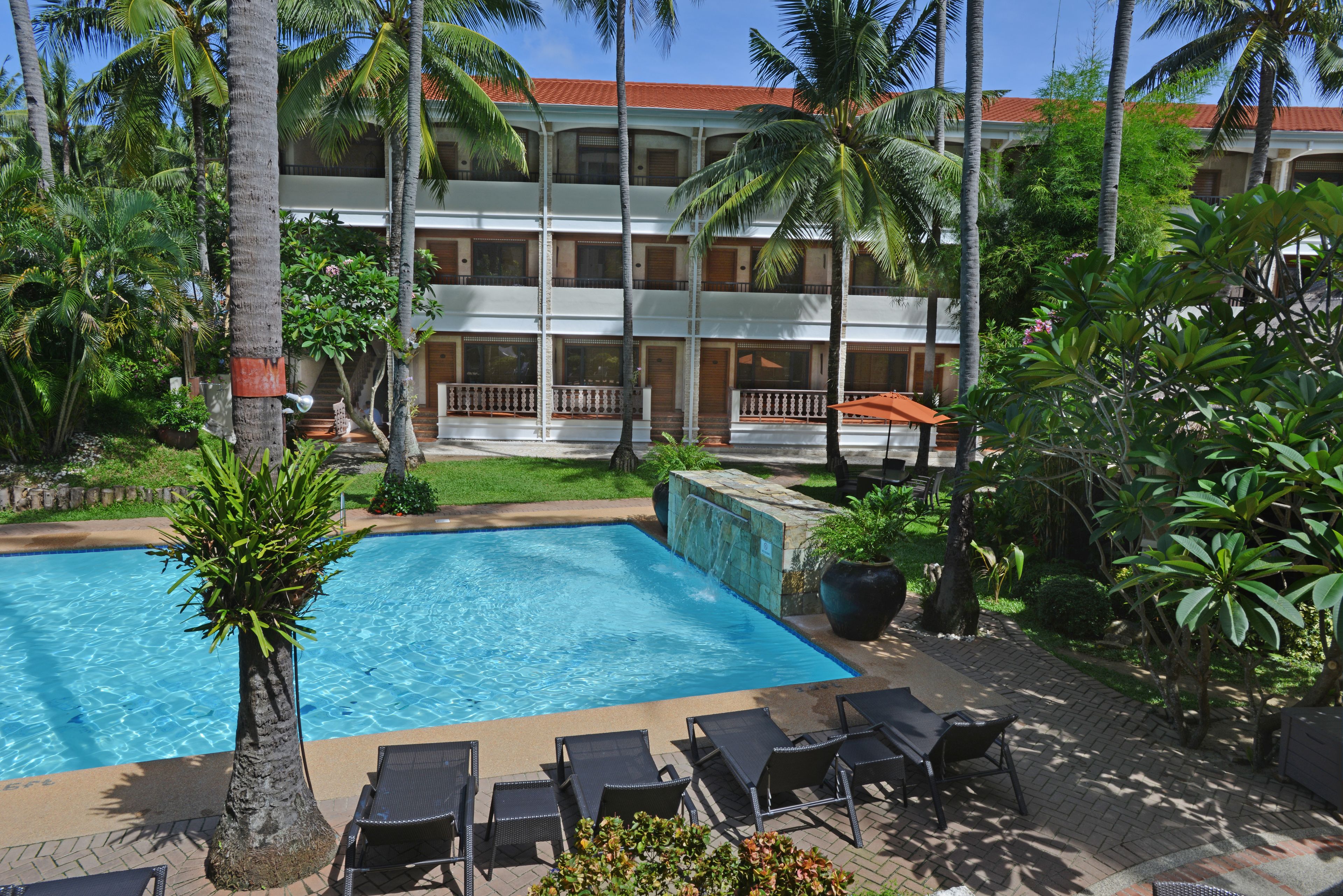 A hotel with a pool, lounge chairs, and palm trees.