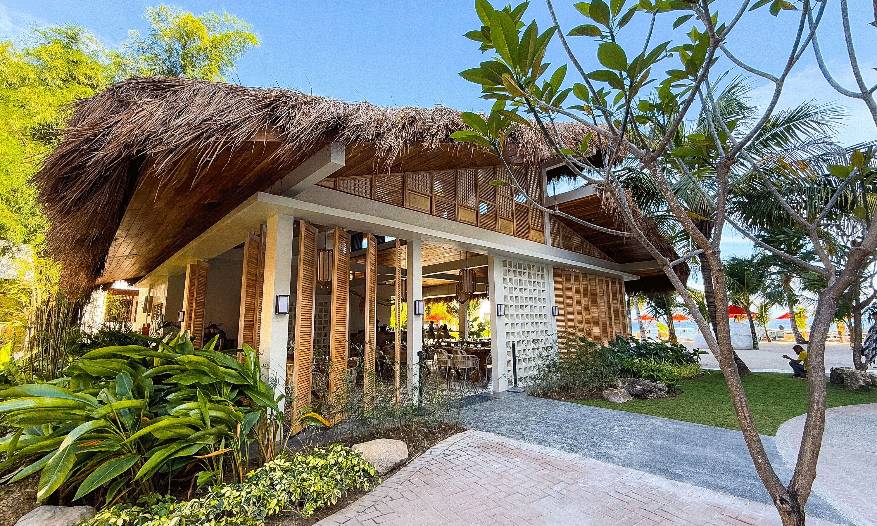 A thatched-roof building with a covered outdoor seating area and lush greenery.