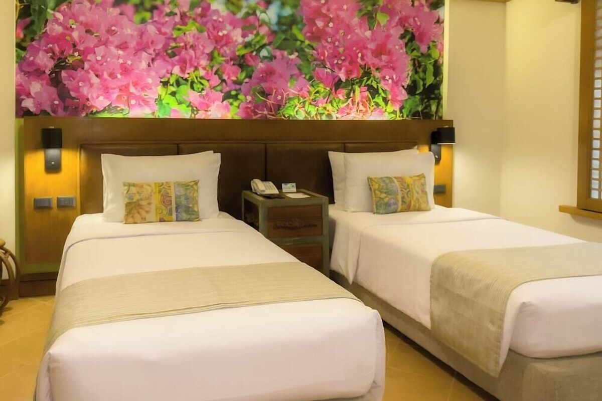 A hotel room with two beds, a nightstand, a telephone, and a wall with a floral mural.
