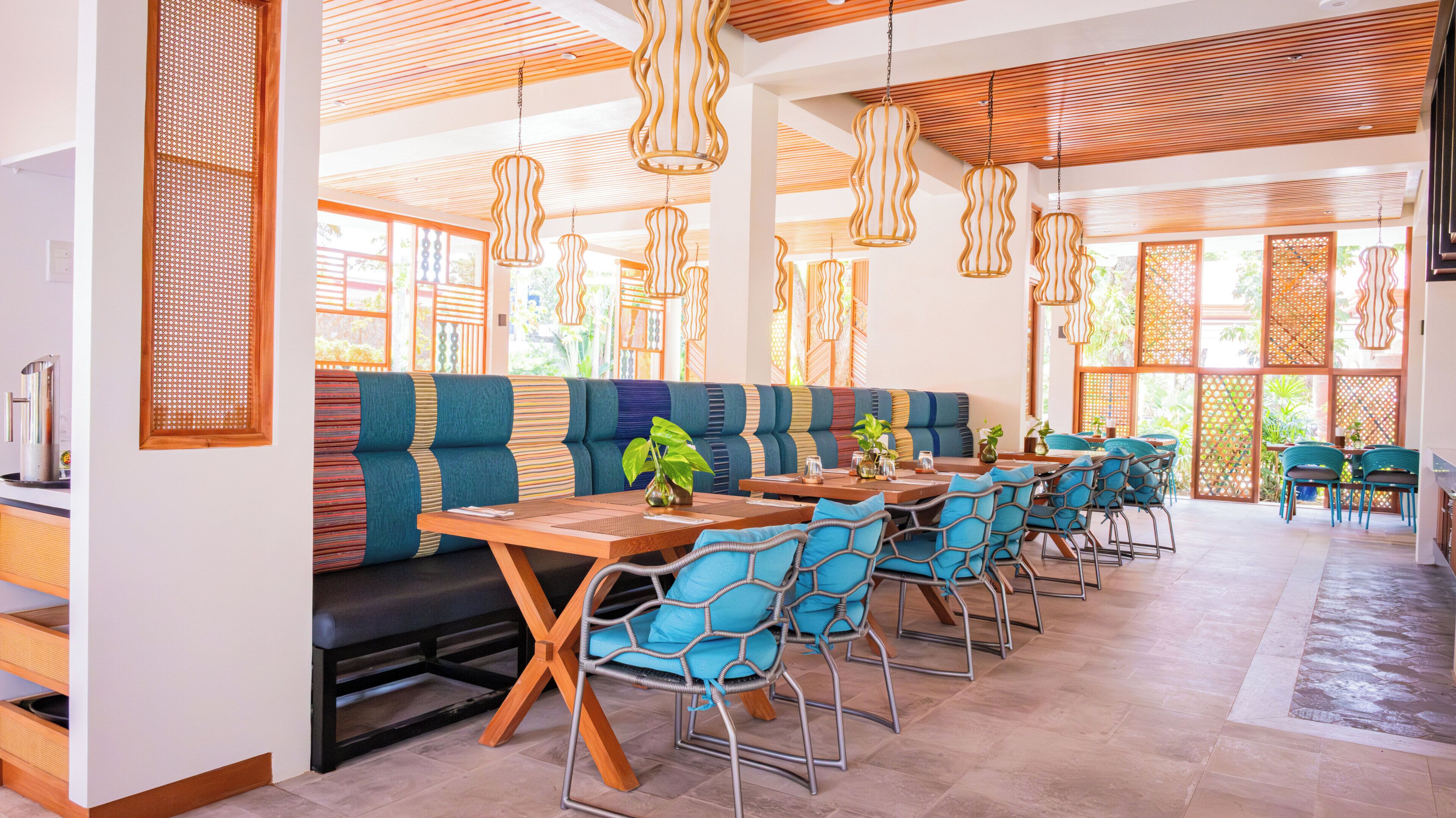 A modern dining area with a long bench, blue chairs, and hanging pendant lights.
