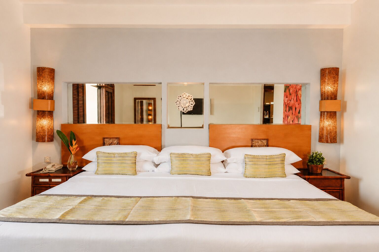A hotel room with a large bed, two nightstands, a mirror, and wall sconces.