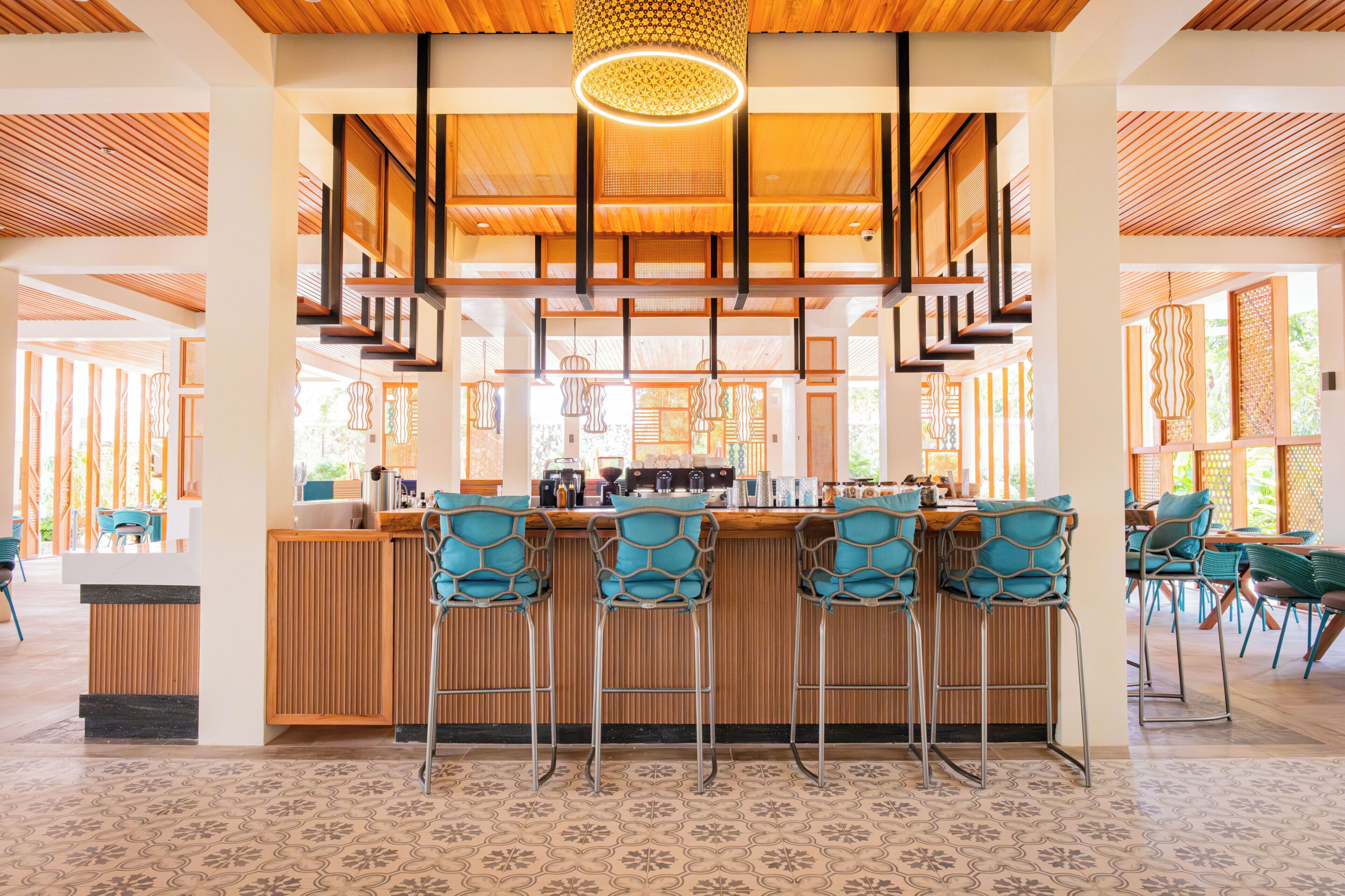 A bar area with a wooden ceiling, patterned floor, and teal chairs.