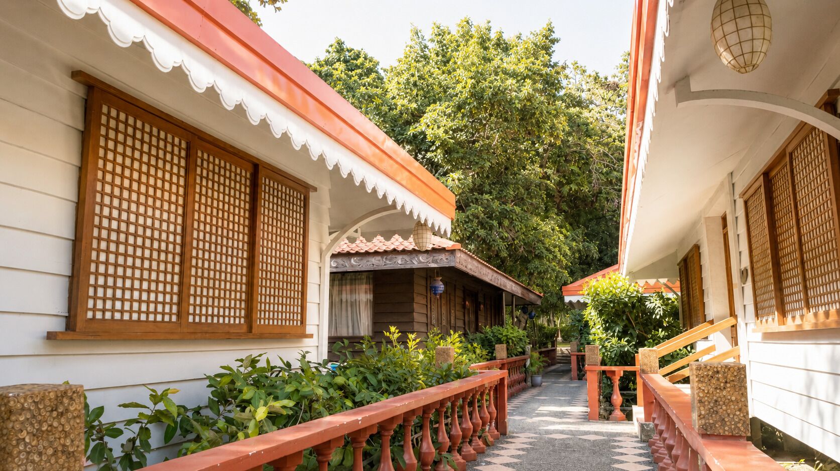 A corridor with traditional wooden doors and windows, surrounded by lush greenery and a tiled floor.