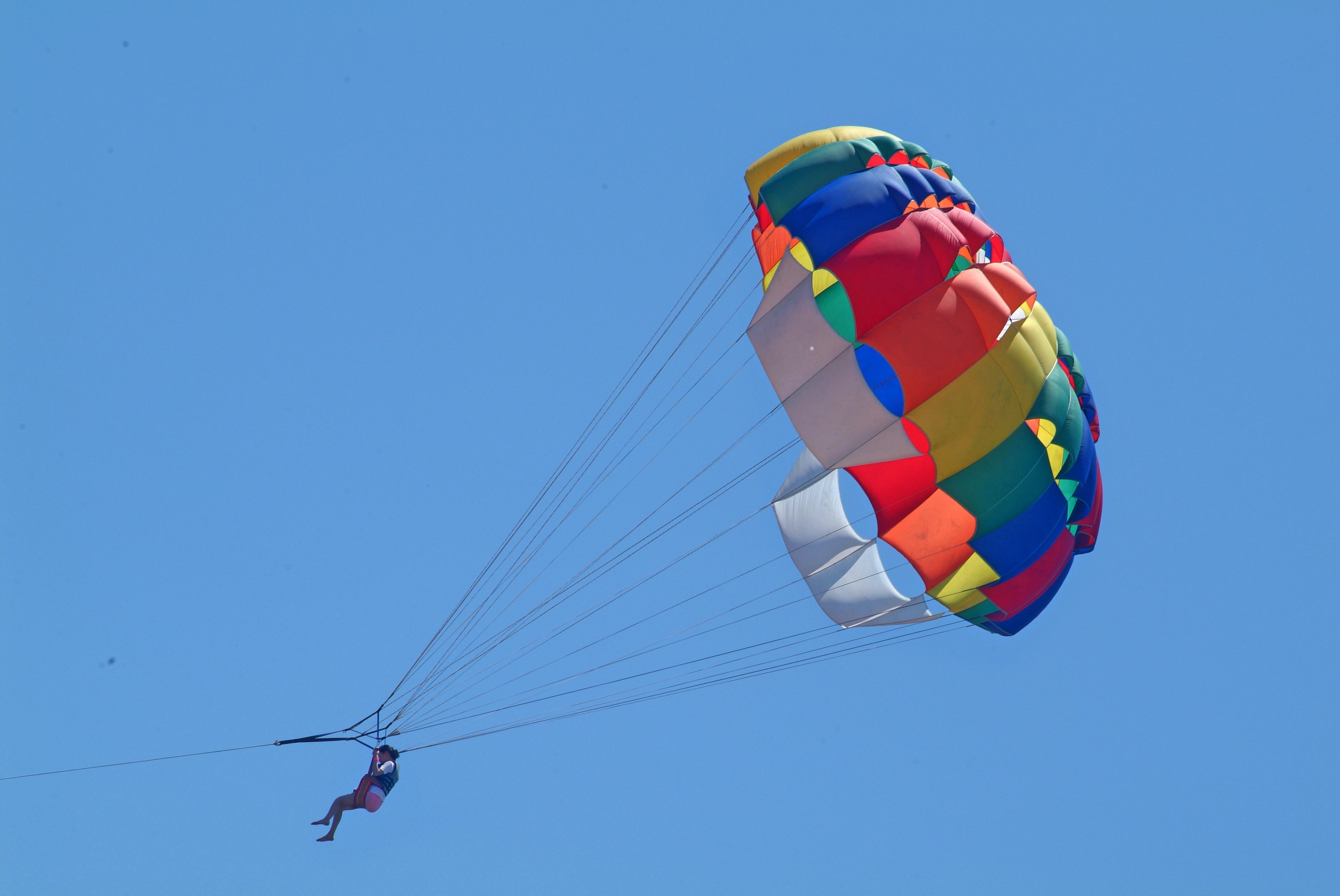 A person skydiving with a colorful parachute against a clear blue sky.
