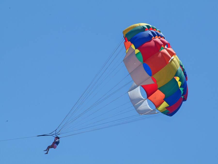 A person skydiving with a colorful parachute against a clear blue sky.