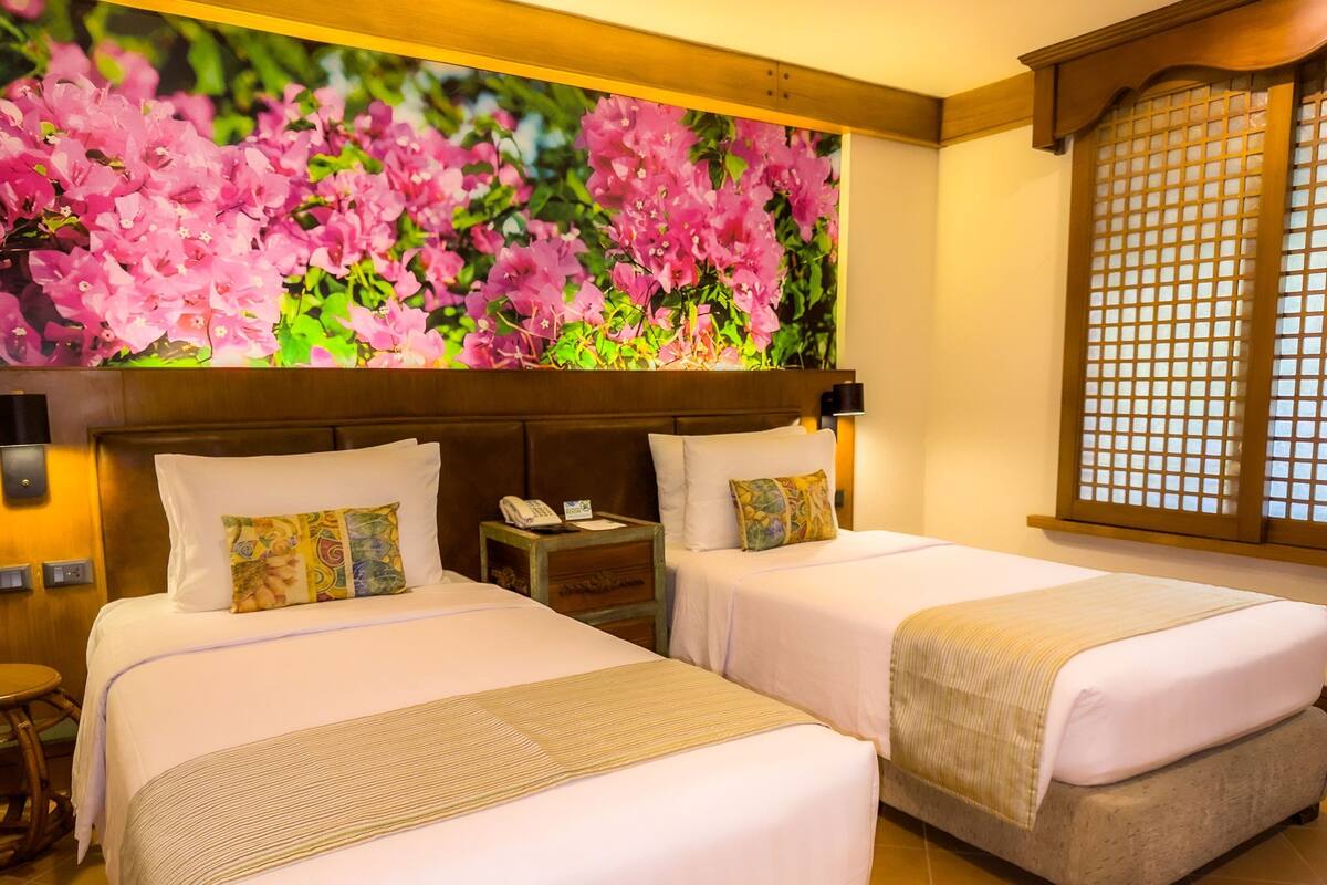 Quarto de hotel com duas camas, uma mesa de cabeceira com telefone e um grande mural floral na parede.