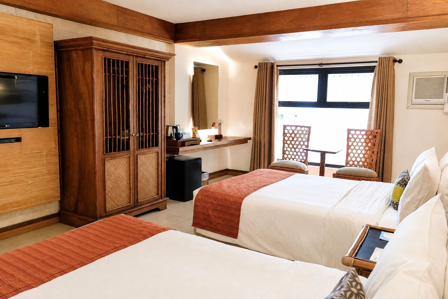 Une chambre d’hôtel avec deux lits, une télévision, un minibar, un bureau et une fenêtre avec des rideaux.