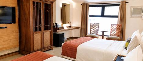 A hotel room with two beds, a TV, a minibar, a desk, and a window with curtains.