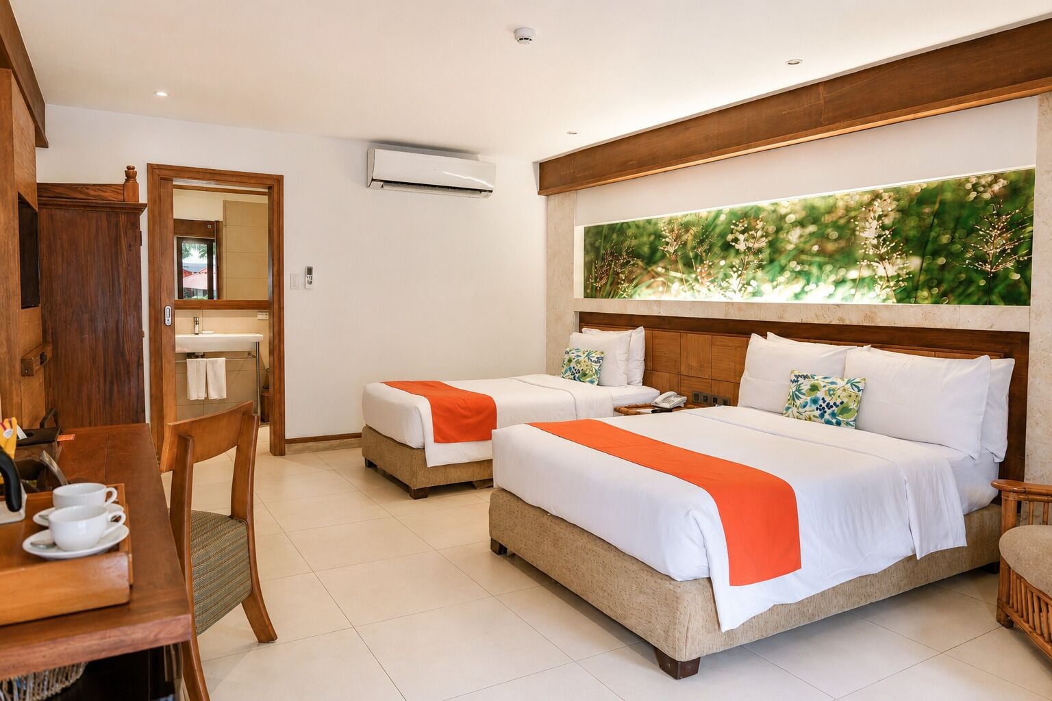 Habitación de hotel con dos camas, un escritorio de madera con una silla, un ventanal con vistas a zonas verdes y un equipo de aire acondicionado.