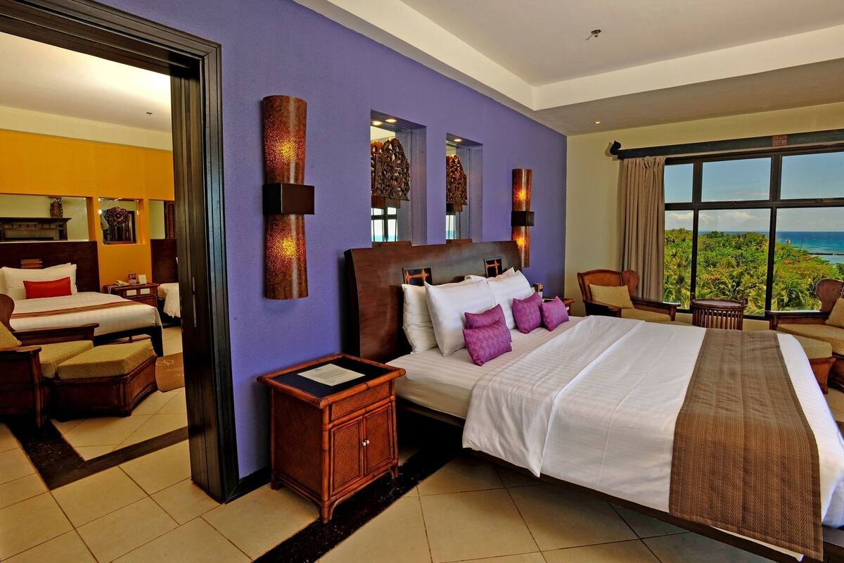 Quarto de hotel com uma cama grande, mesa de cabeceira, armário de madeira e vista para o mar.