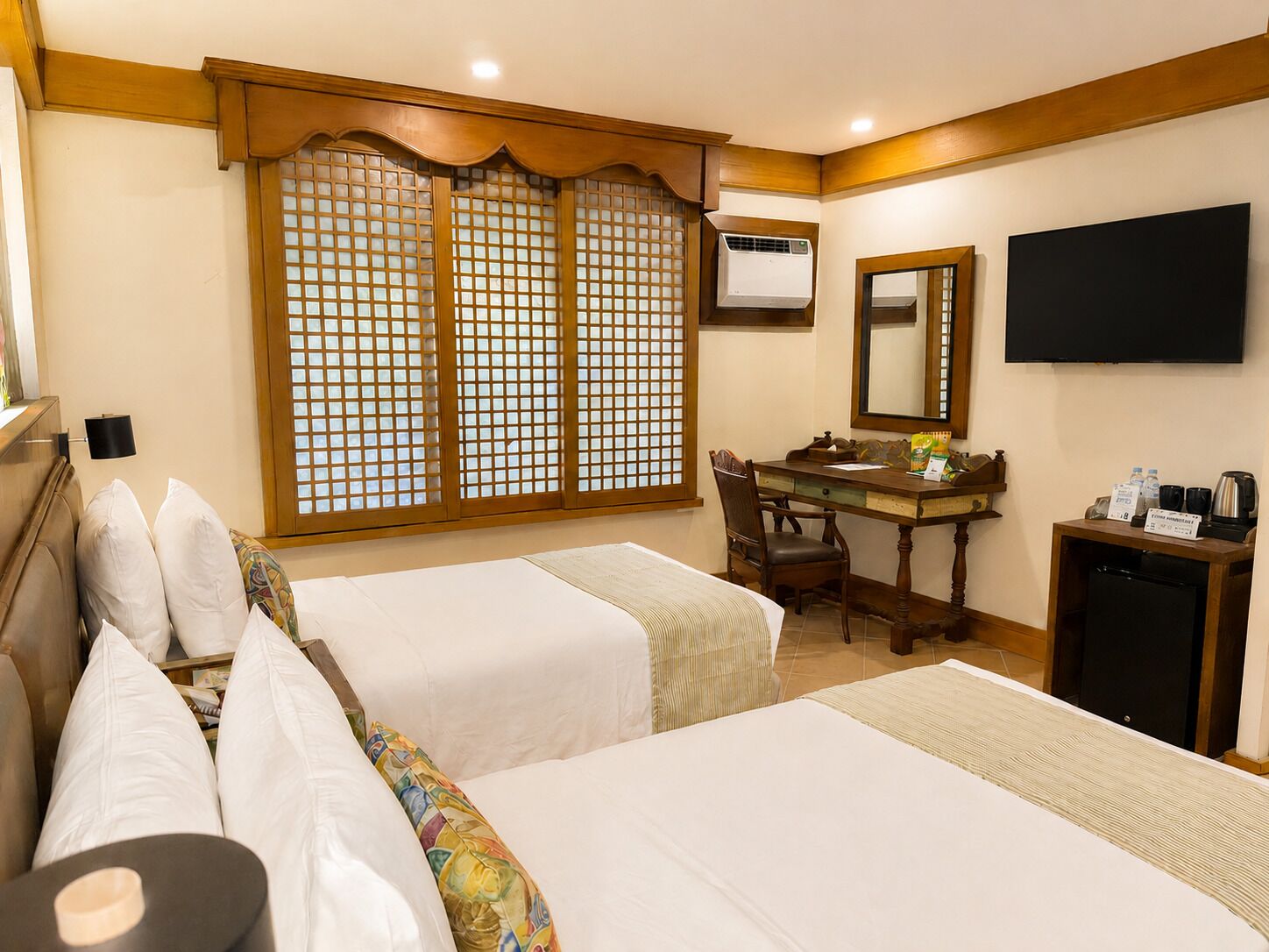 A hotel room with two beds, a desk, a chair, a television, and a minibar.