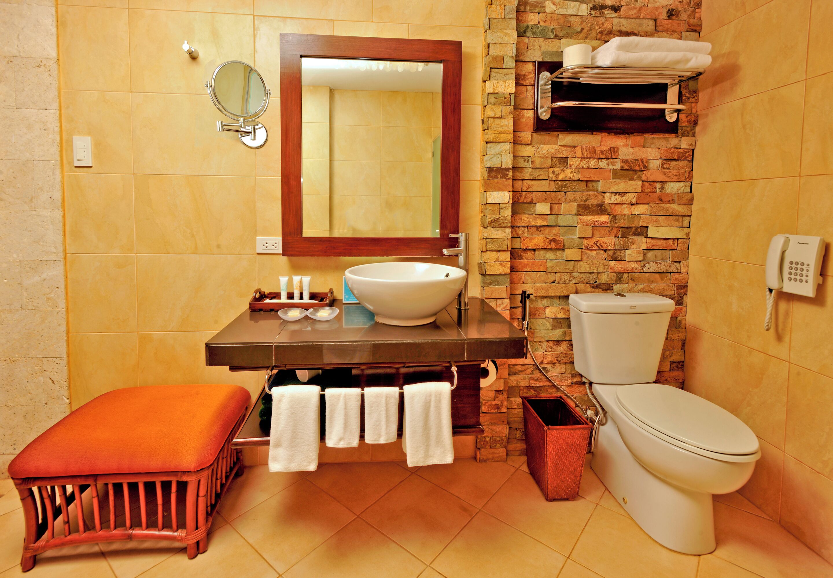 Une salle de bain équipée d’un lavabo, d’un miroir, de toilettes et d’un banc.