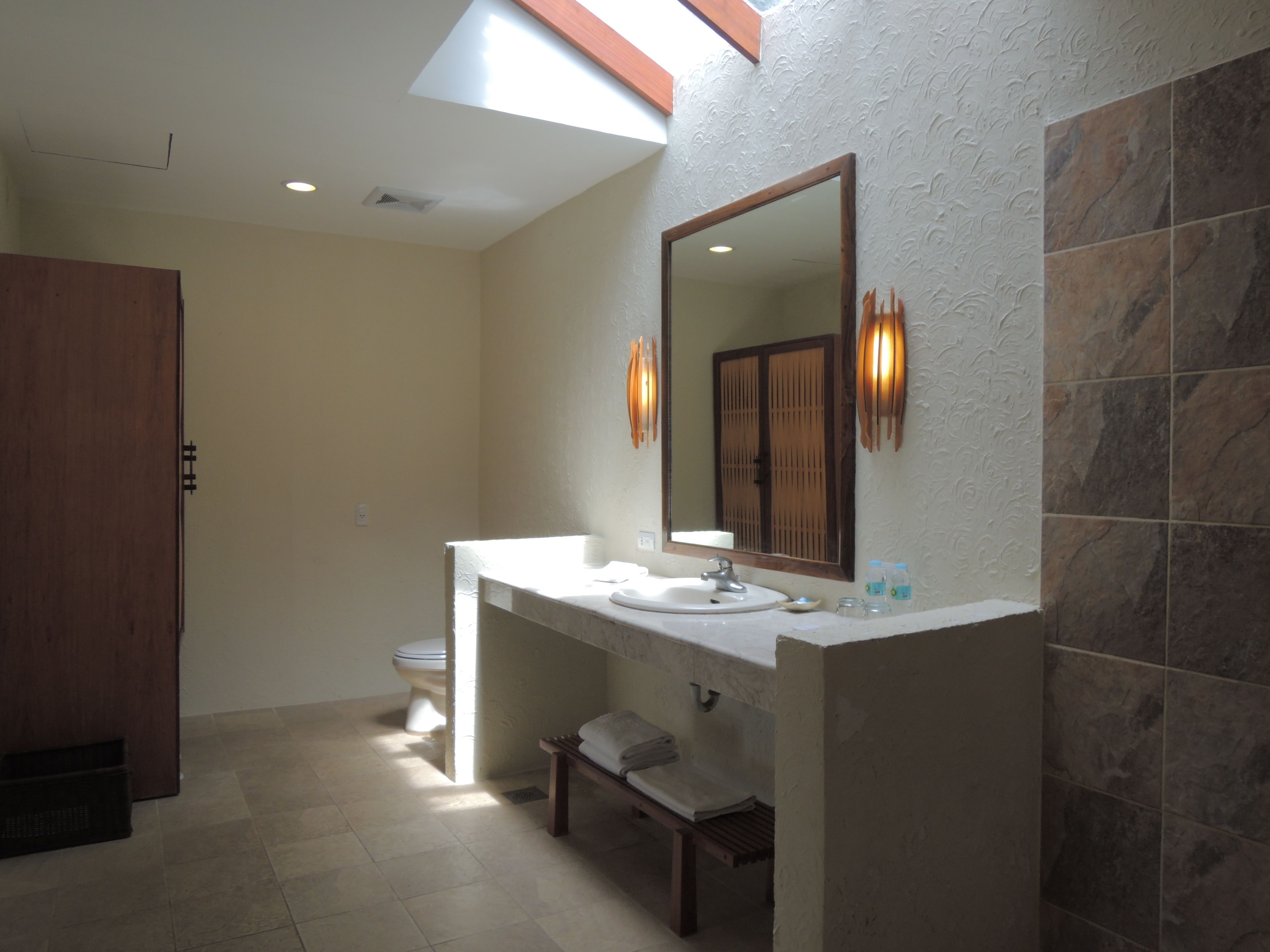 A modern bathroom with a skylight, a large mirror, a vanity with a sink, and a toilet.