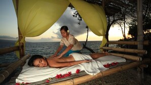 Una persona recibiendo un masaje en una cama de bambú con vista al mar.