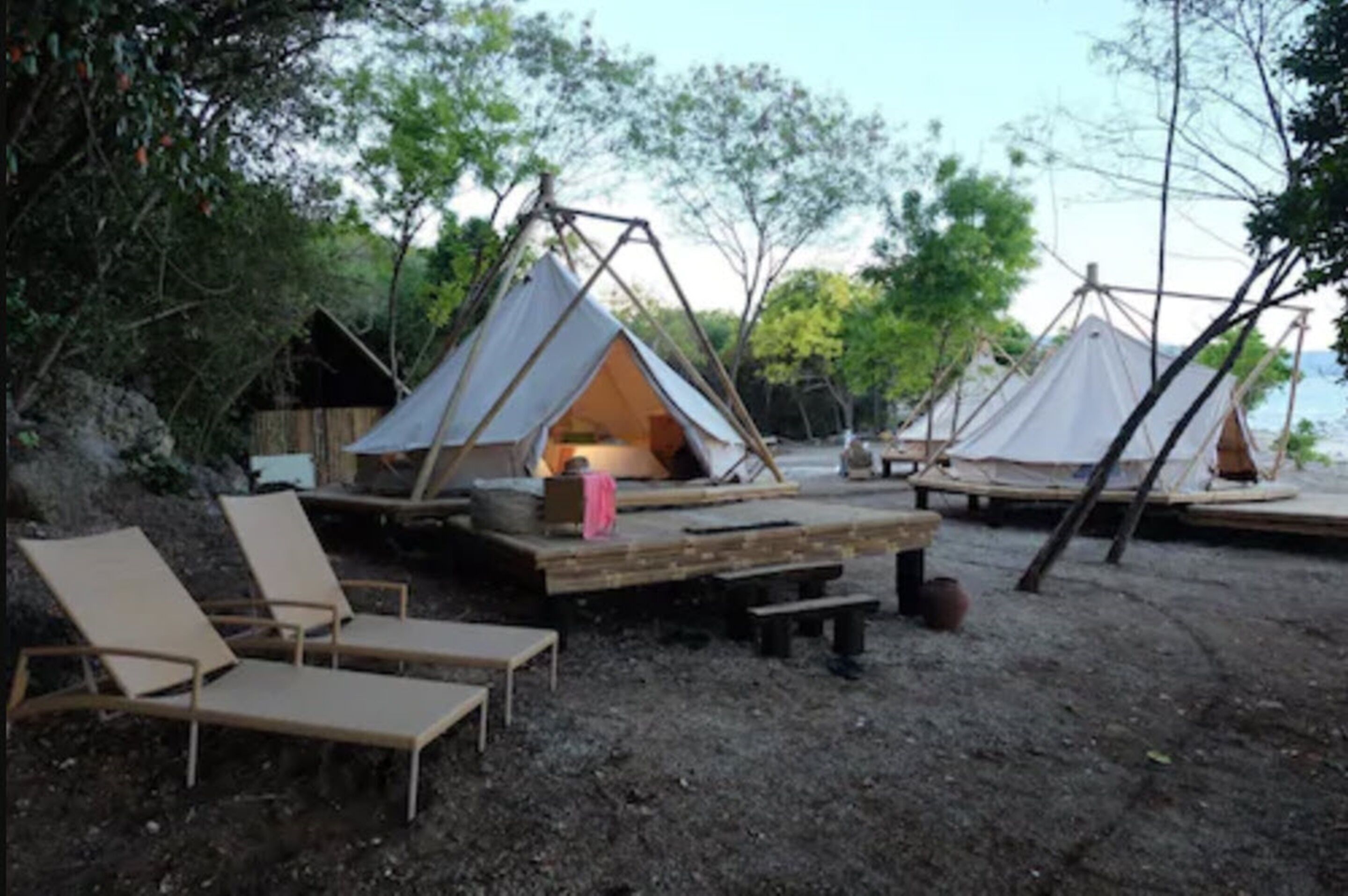 A campsite with two tents, a wooden deck, and lounge chairs.