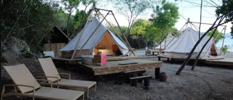 A campsite with two tents, a wooden deck, and lounge chairs.