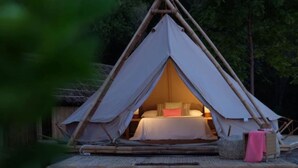 Una tienda de campaña con una cama en su interior, rodeada por una terraza de madera y árboles.