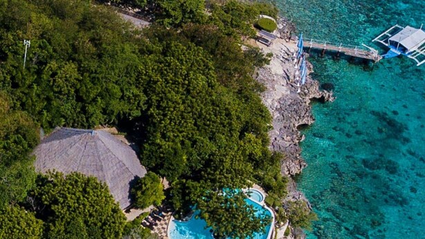 Vista aérea de una isla tropical con piscina rodeada de exuberante vegetación y aguas turquesas cristalinas.