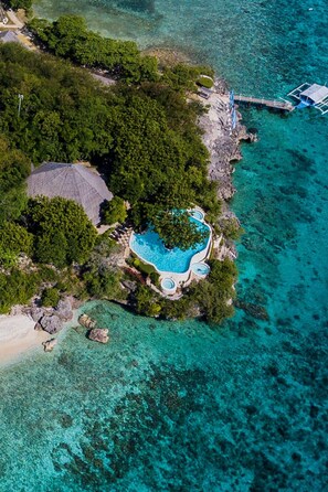 An aerial view of a tropical island with a swimming pool surrounded by lush greenery and clear turquoise waters. - Bluewater Sumilon Island Resort (Oslob)
