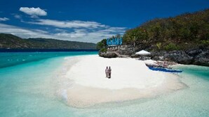 Una playa con aguas turquesas cristalinas, una orilla de arena blanca y una pequeña estructura con señalización azul.