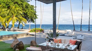 A beachside dining area with wicker furniture, a pool, and palm trees. - Atmosphere Resorts & Spa (Dauin)