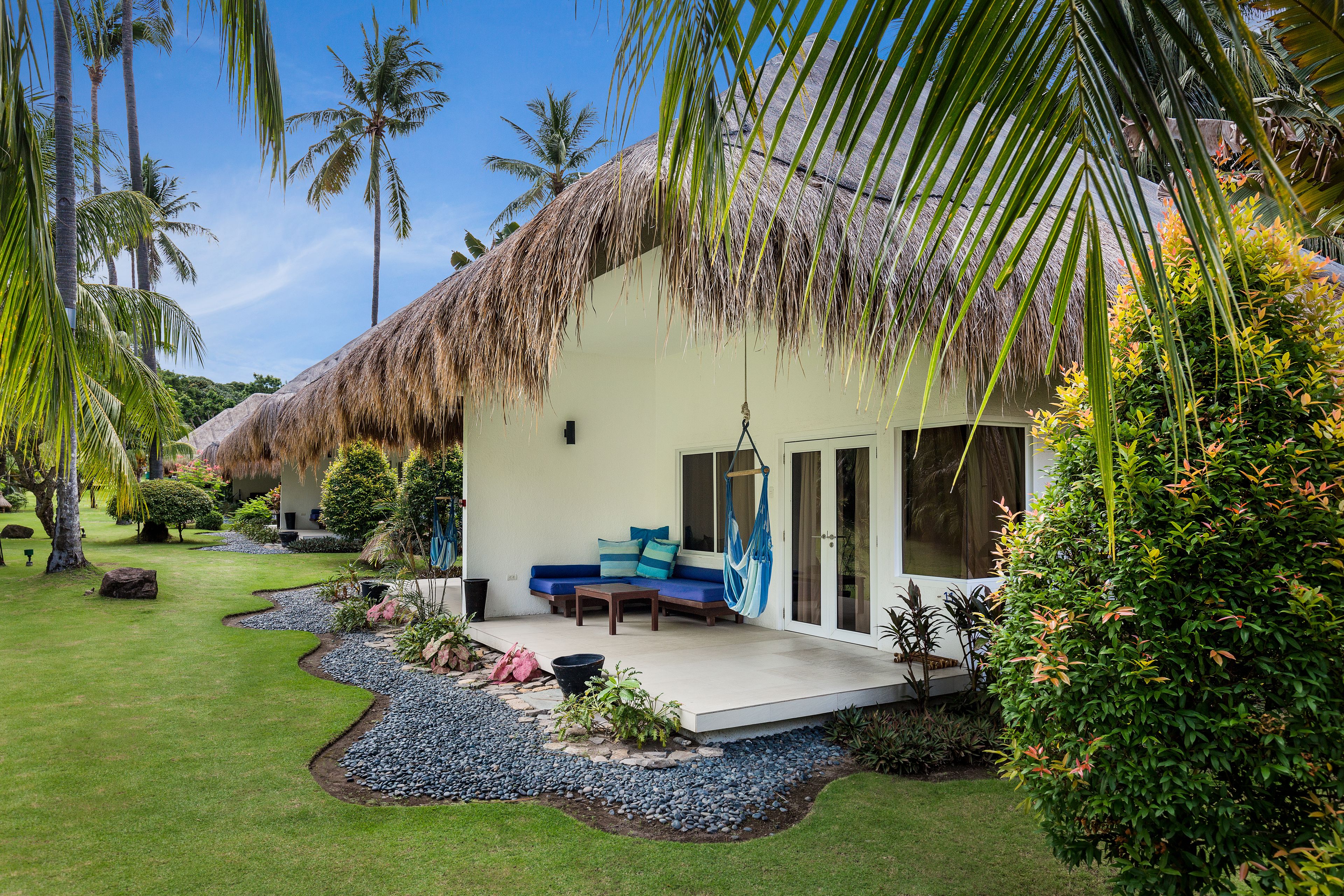 A thatched-roof house with a patio, a hammock, and a seating area.