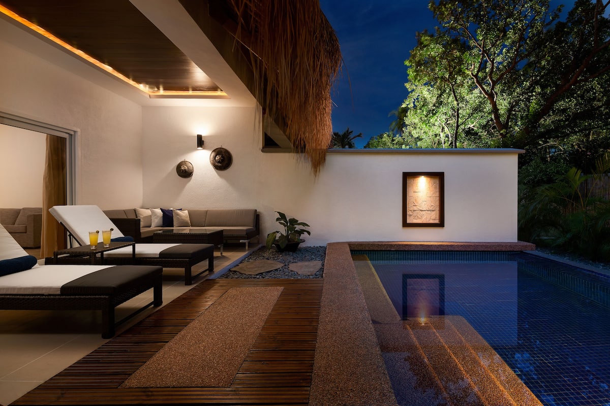 A modern outdoor lounge area with a pool, seating, and a framed artwork on the wall.