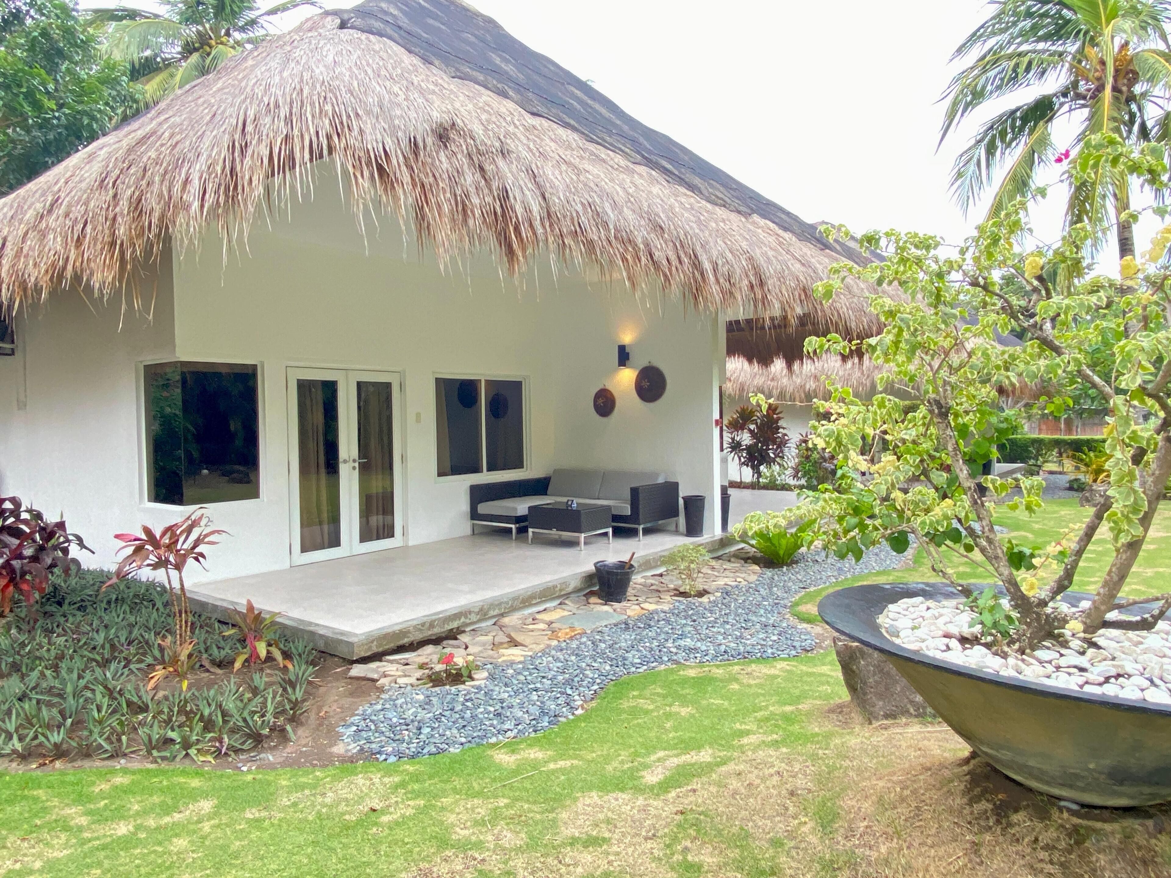 A modern house with a thatched roof, a patio with outdoor furniture, and a garden with various plants.