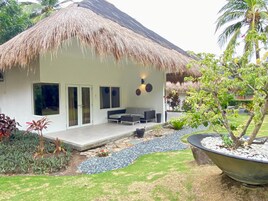 A modern house with a thatched roof, a patio with outdoor furniture, and a garden with various plants.