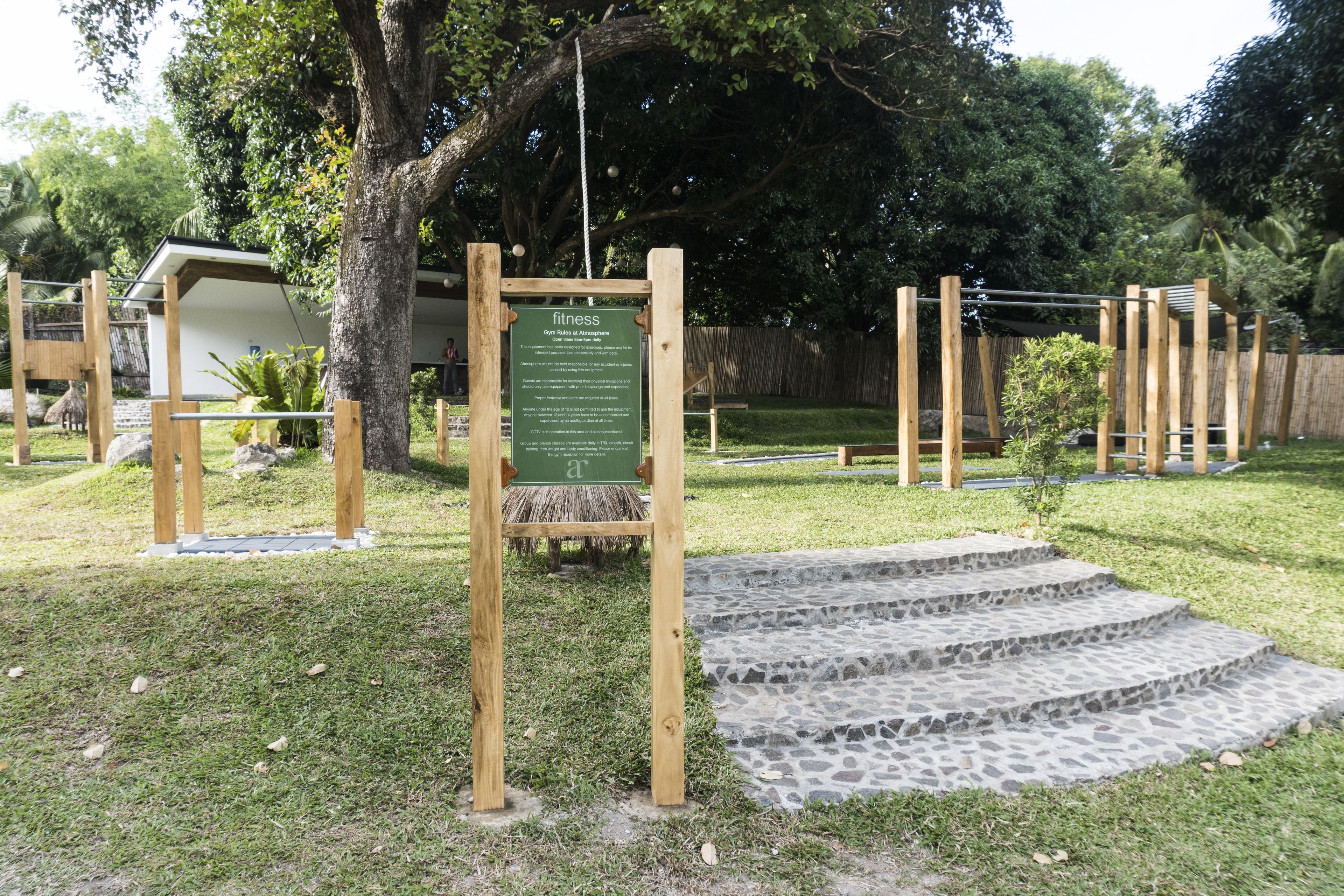 Un panneau en bois avec une inscription, un petit escalier en pierre et une zone herbeuse avec des arbres.