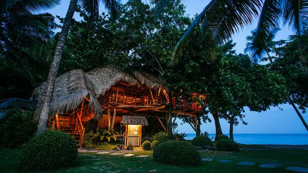 A thatched-roof hut with a wooden deck, surrounded by lush greenery and palm trees, overlooking the ocean. - Atmosphere Resorts & Spa (Dauin)