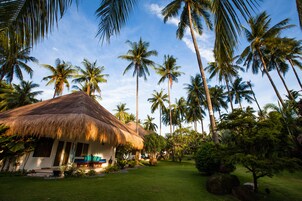 A thatched-roof house with a lawn and palm trees.