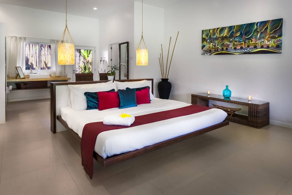 A spacious bedroom with a large bed, bedside tables, a mirror, and a painting on the wall.