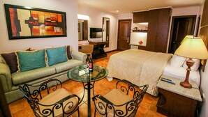A hotel room with a bed, a sofa, a dining table, and a TV. - Royal Bellagio Hotel (Makati)