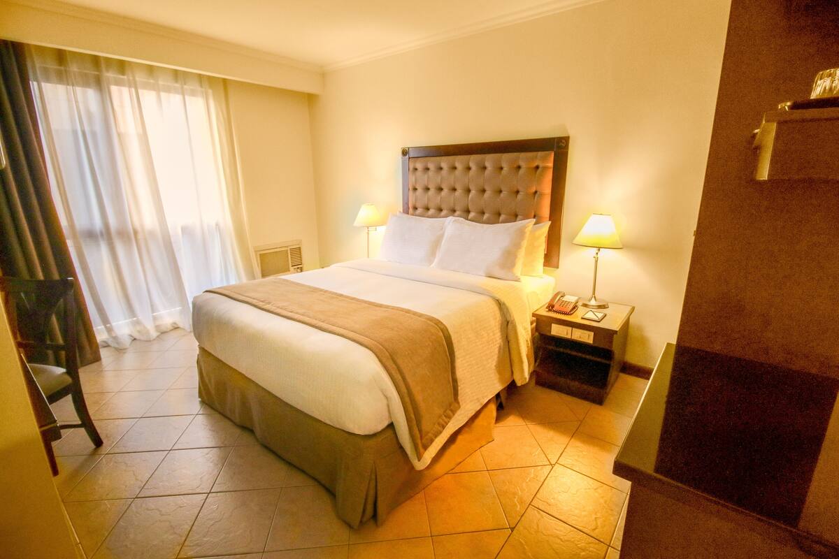 A hotel room with a large bed, two bedside tables, a chair, and a bathroom.