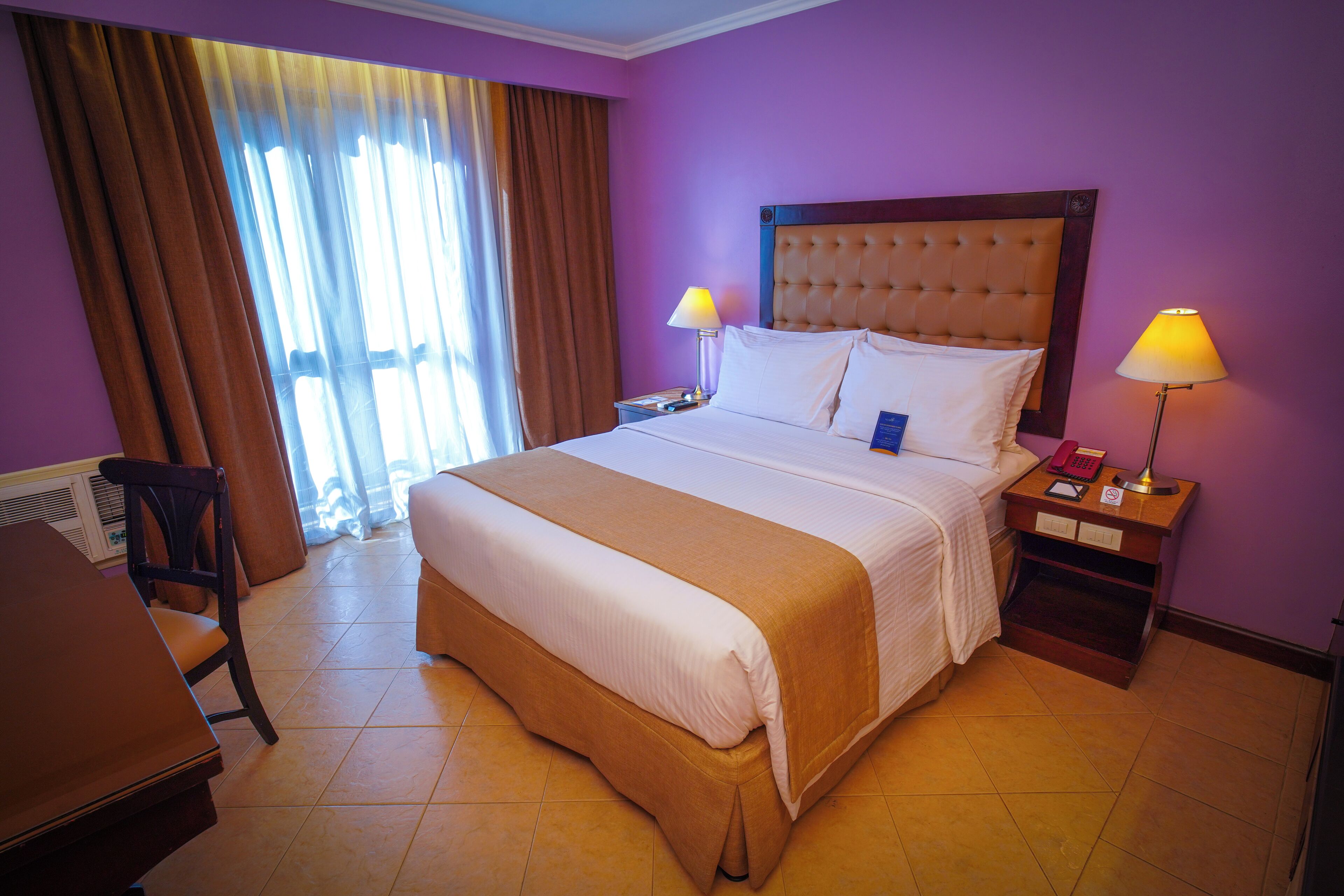 Una habitación de hotel con una cama grande, dos mesitas de noche con lámparas, una silla y un escritorio.