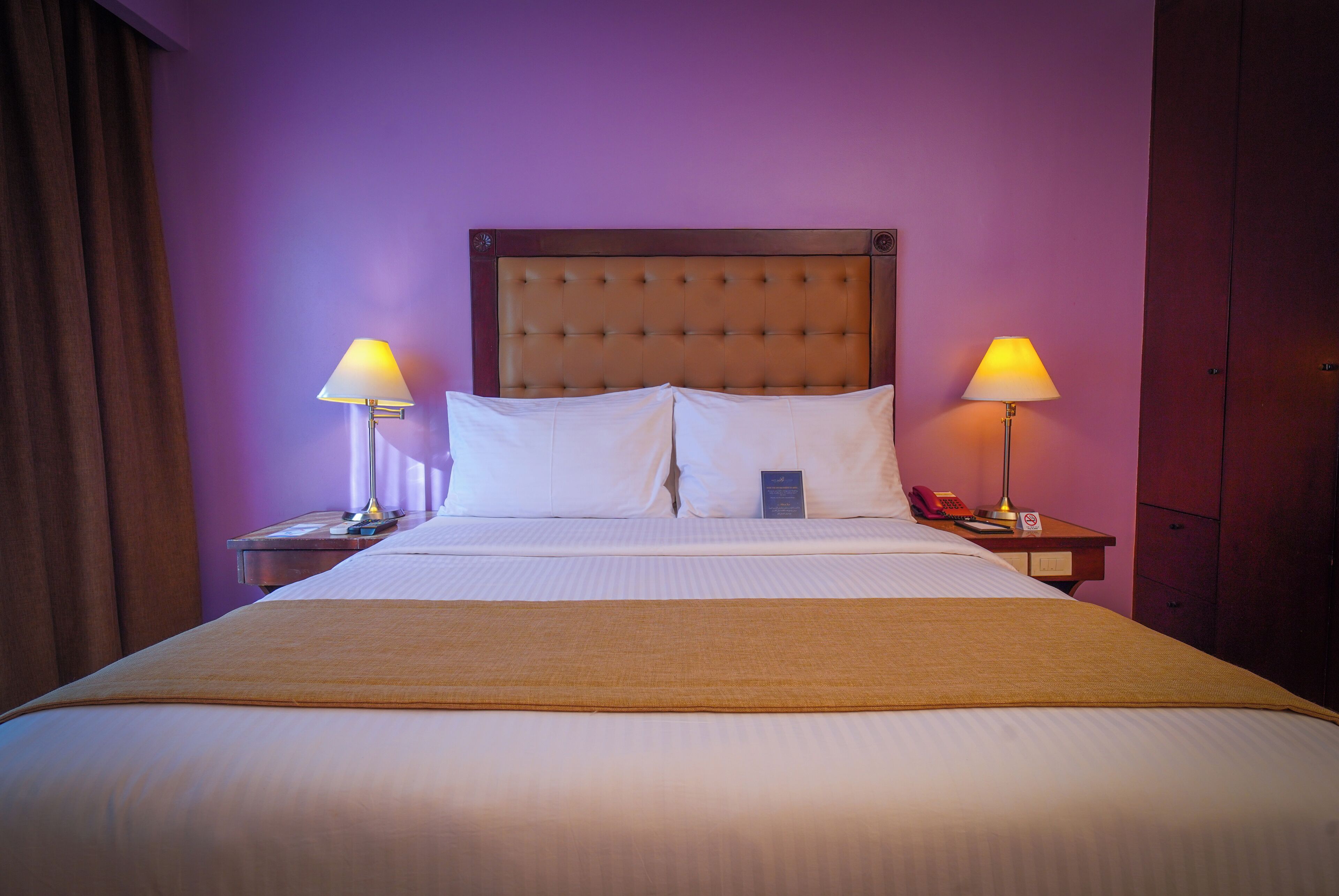 A hotel room with a large bed, two bedside tables, and two lamps.