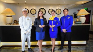A reception area with a black counter, four staff members in uniform, and clocks on the wall. - Royal Bellagio Hotel (Makati)