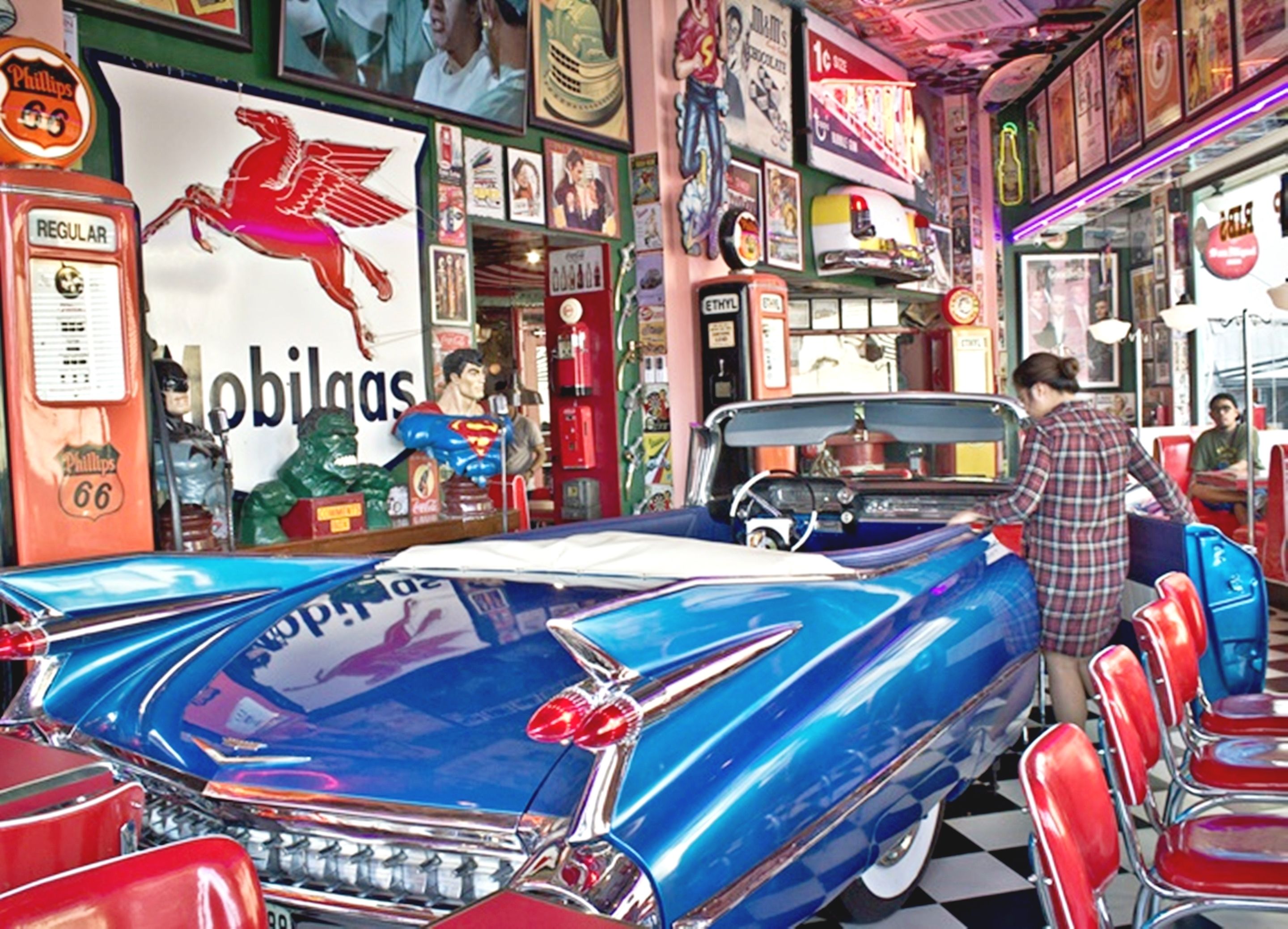 A vintage car in a diner setting with neon signs and classic decor.