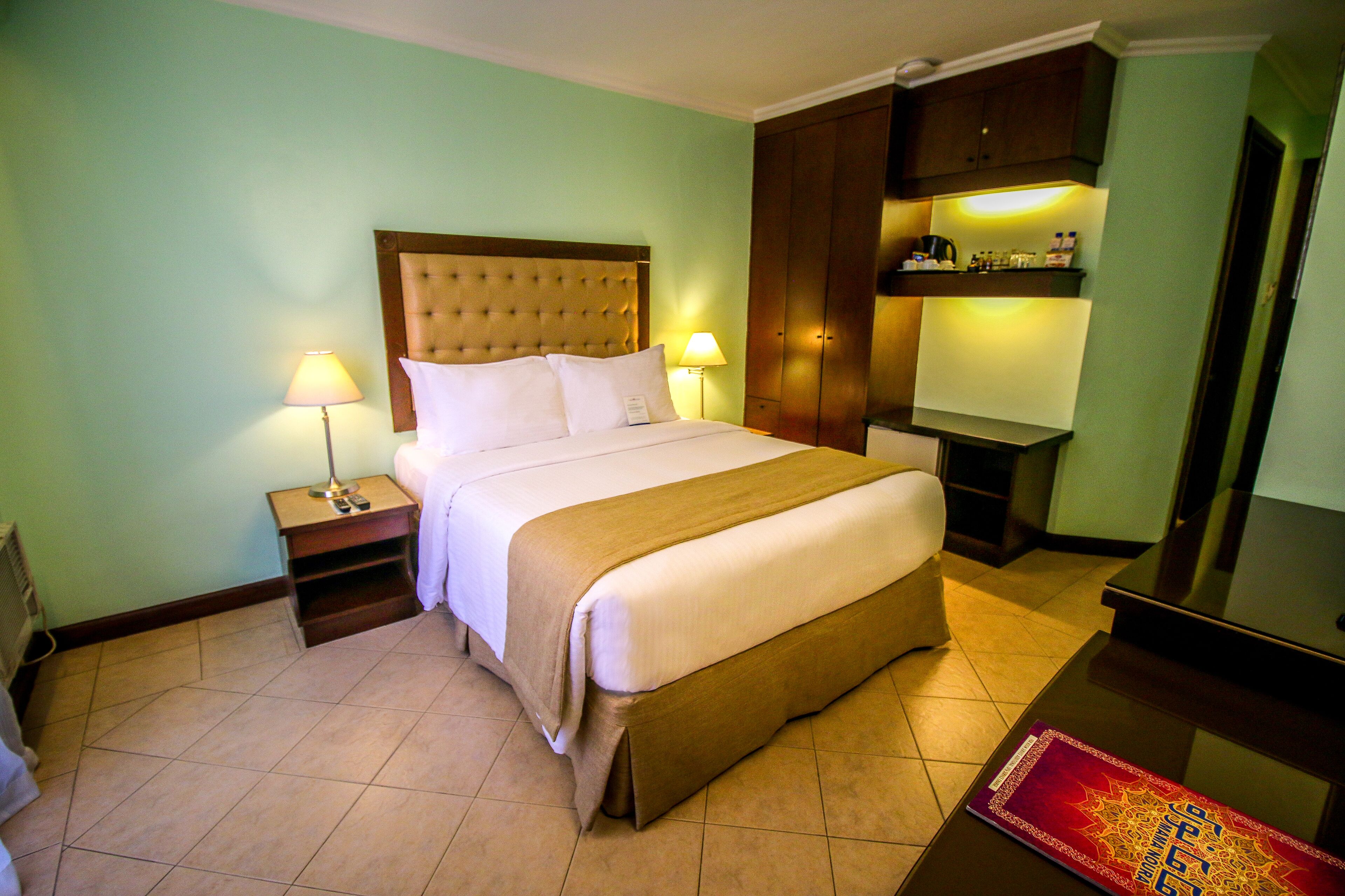 A hotel room with a large bed, two bedside lamps, a wooden headboard, a television, and a minibar.