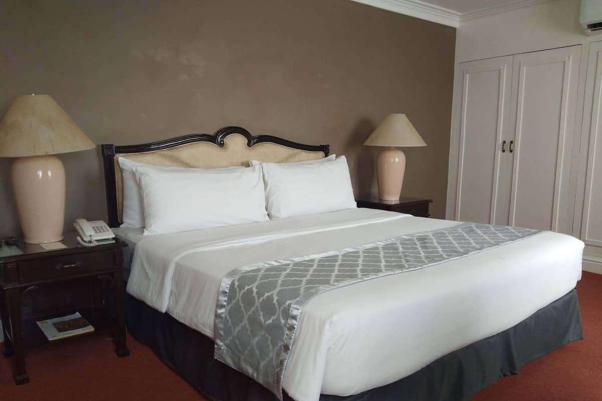 A neatly made bed with a patterned bedspread, two bedside lamps, a telephone, and a wardrobe in a hotel room.