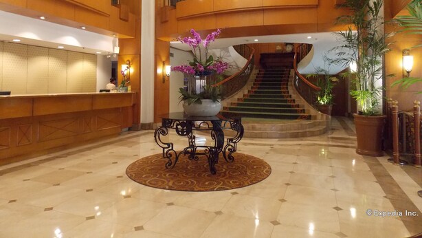 Un vestíbulo espacioso con una recepción, una escalera y plantas decorativas.