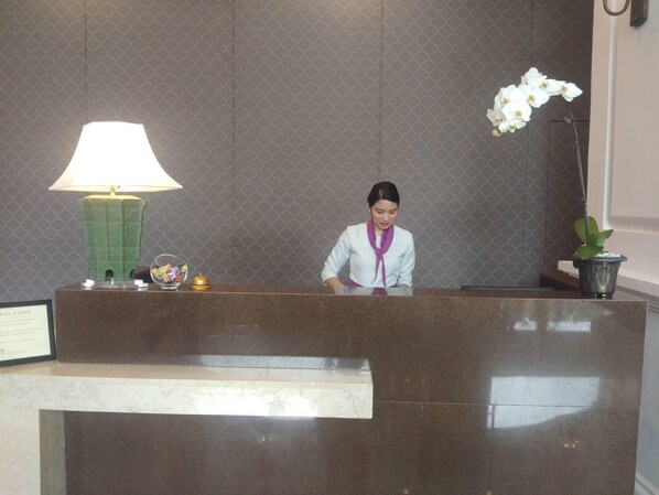 A reception desk with a marble counter, a green lamp, a framed certificate, and a potted plant.