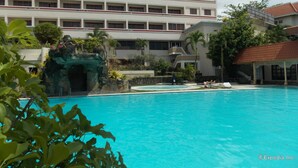Un hotel con piscina, jardín de rocas y un edificio de varios pisos con balcones.
