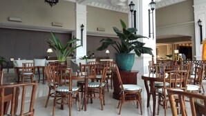 Un vestíbulo amplio con techos altos, columnas ornamentadas y diversas opciones de asientos, incluyendo sillas y mesas de madera.