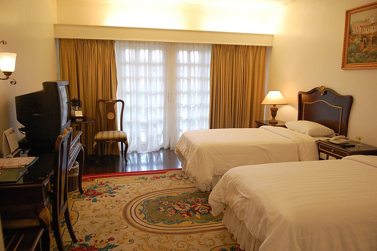 Une chambre d’hôtel avec deux lits, une télévision, un bureau avec une lampe et une chaise.