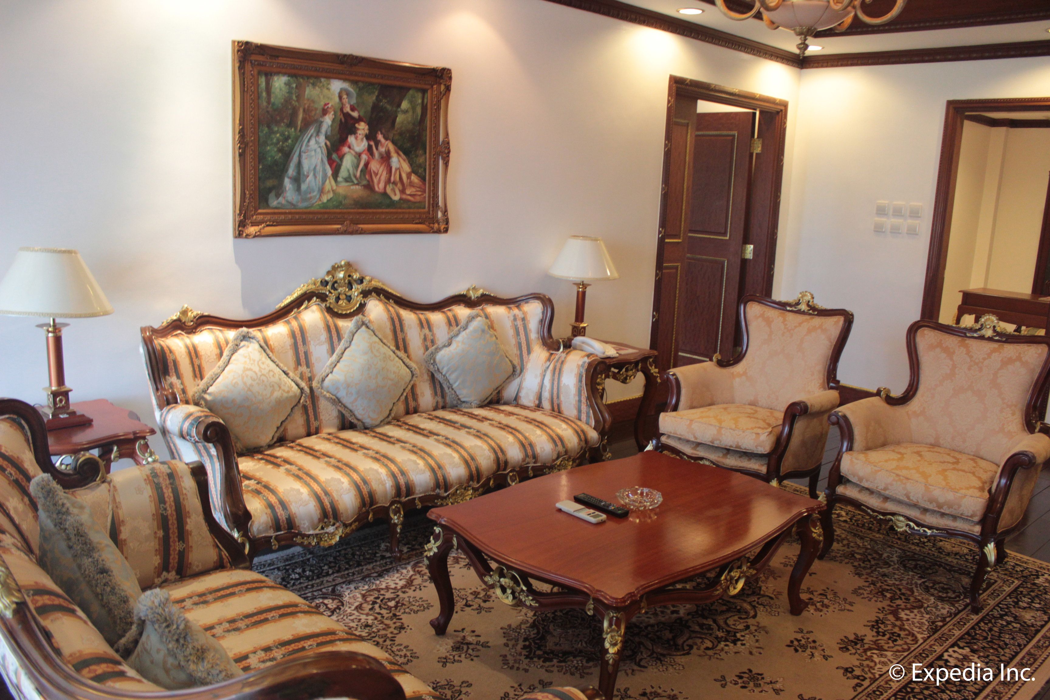 A traditional sitting room with a sofa, two armchairs, a coffee table, and a painting on the wall.