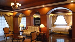 A hotel room with a large bed, a sofa, two armchairs, a coffee table, and a TV. - Fort Ilocandia Resort Hotel (Laoag)