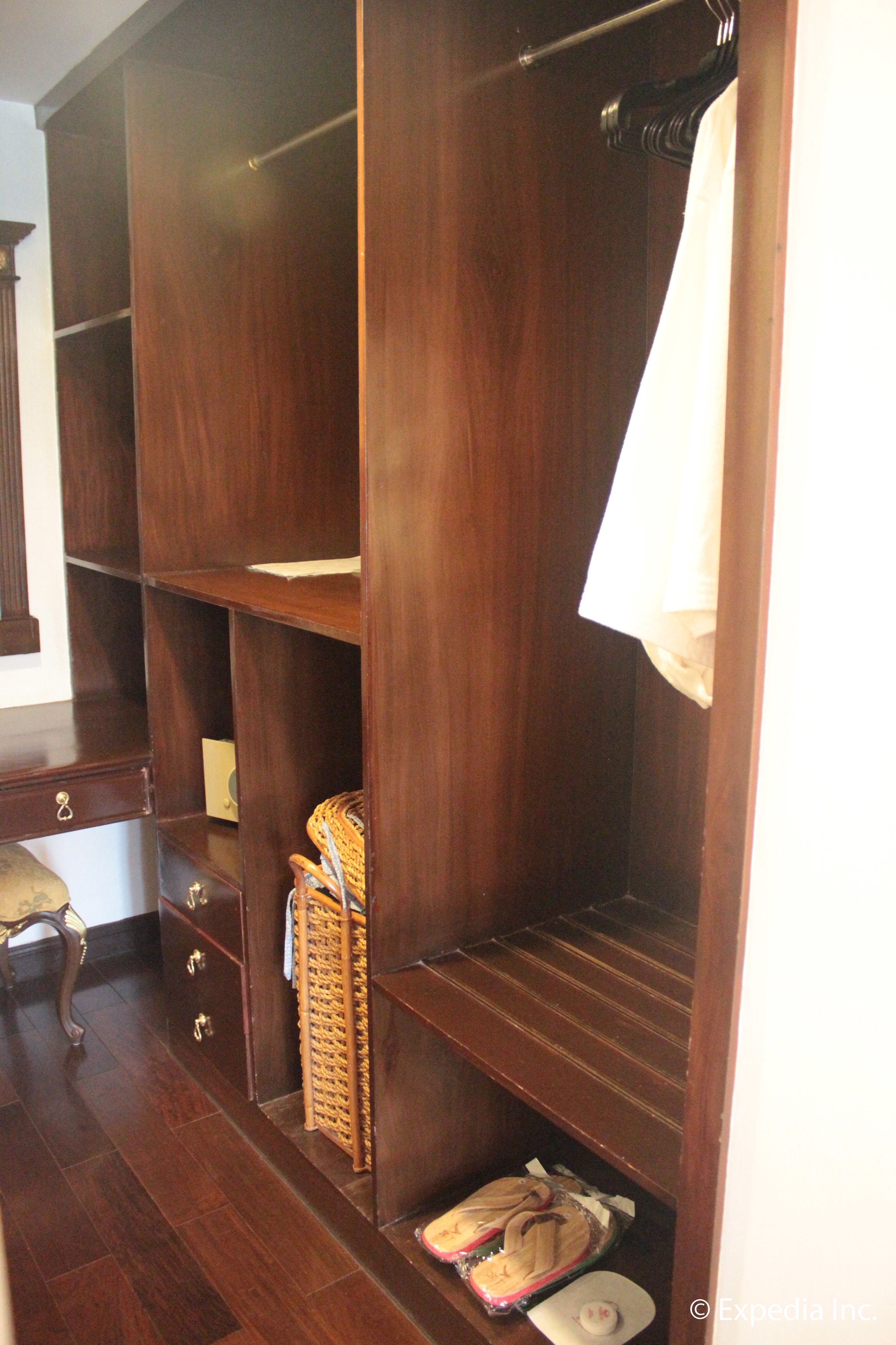 A wooden wardrobe with multiple shelves and drawers, a wicker basket, and a small white object on the floor.